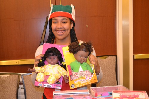 Volunteer elf Makia all smiles, shows two Black dolls.