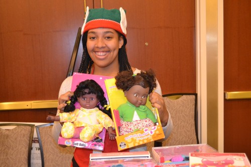 Volunteer elf Makia all smiles, shows two Black dolls.