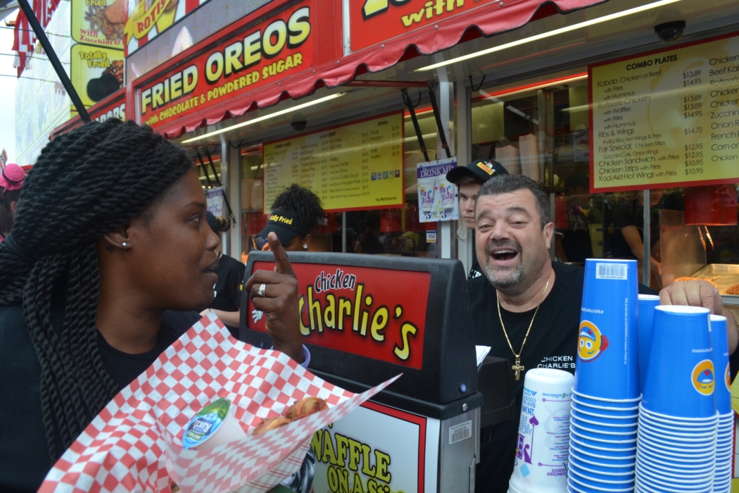 The man himself Chicken Charlie, works behind the counter at the fair talking to and servicing fairgoer.